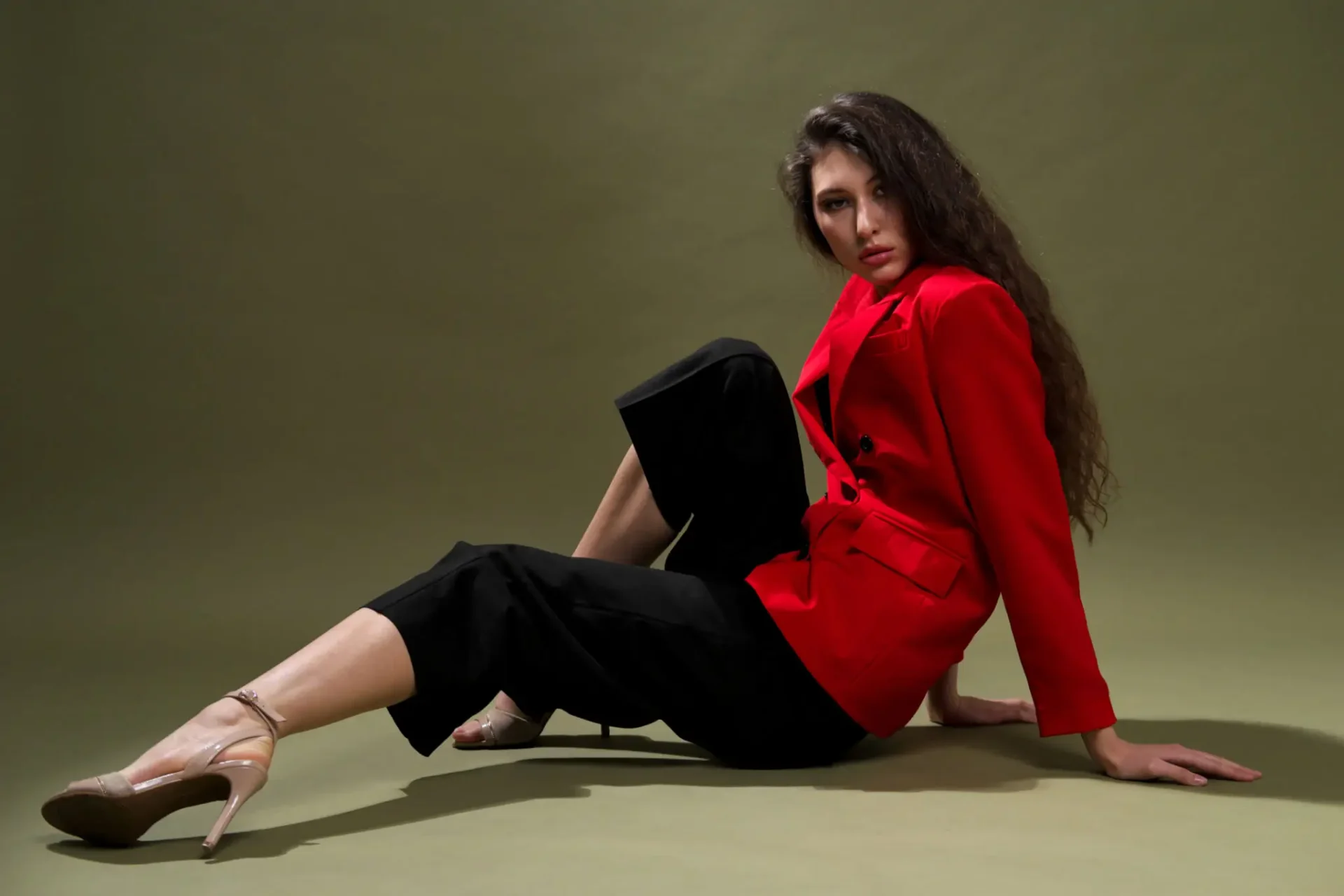 Woman posing in red jacket, green background.